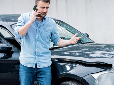 Ein Mann steht neben einem beschädigten Auto und telefoniert.